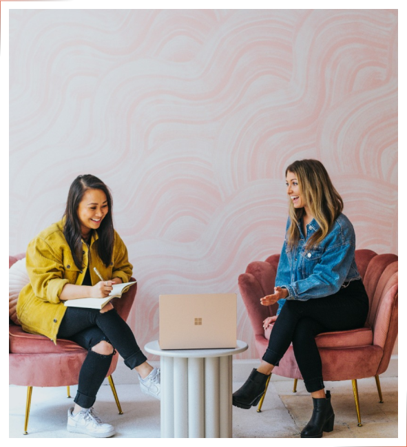 Two women sitting in pink chairs, doing a therapy session while Nebo is on their laptop writing Progress Notes.